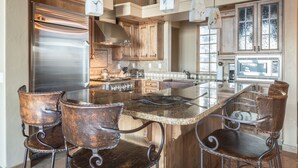 A kitchen with a large island, stainless steel appliances, and rustic bar stools. - Moonlight Basin | Ski-In/ Out | Hot Tub (Big Sky)