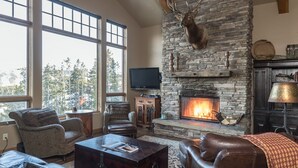 A cozy living room with a stone fireplace, leather furniture, and a mounted deer head. - Moonlight Basin | Ski-In/ Out | Hot Tub (Big Sky)