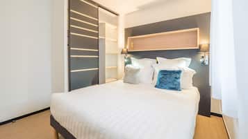 Une chambre d’hôtel moderne avec un grand lit, un dressing et une tête de lit en bois.
