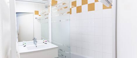 Un baño moderno con lavamanos blanco, espejo y ducha con cerramiento de vidrio.