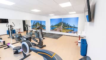 Een sportschool met diverse fitnessapparaten, een grote spiegel en sfeervolle wanddecoratie.