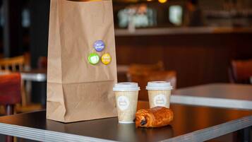 Un sac en papier orné de symboles de recyclage, deux tasses à café et un croissant sur une table.