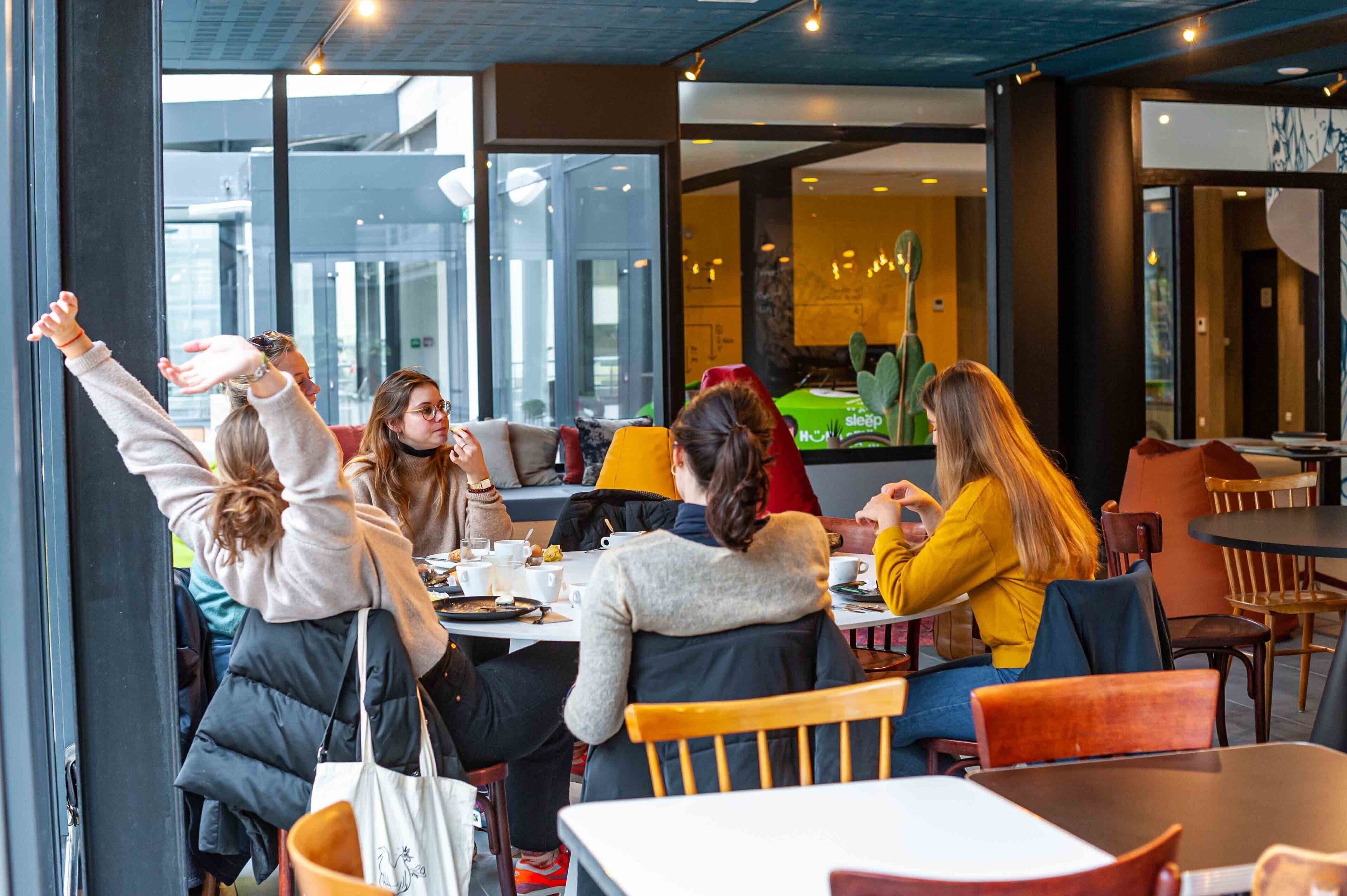 A group of people seated around a table in a modern cafe with large windows and a view of the cityscape.