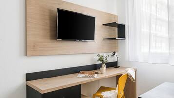 Ein modernes Hotelzimmer mit Schreibtisch aus Holz, einem Flachbildfernseher, einer kleinen Pflanze und einem gelben Stuhl.