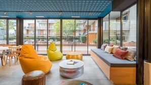 Una sala de estar moderna con sofá, sillón tipo bean bag y mesa de centro, ventanas amplias con vistas al patio y edificios.