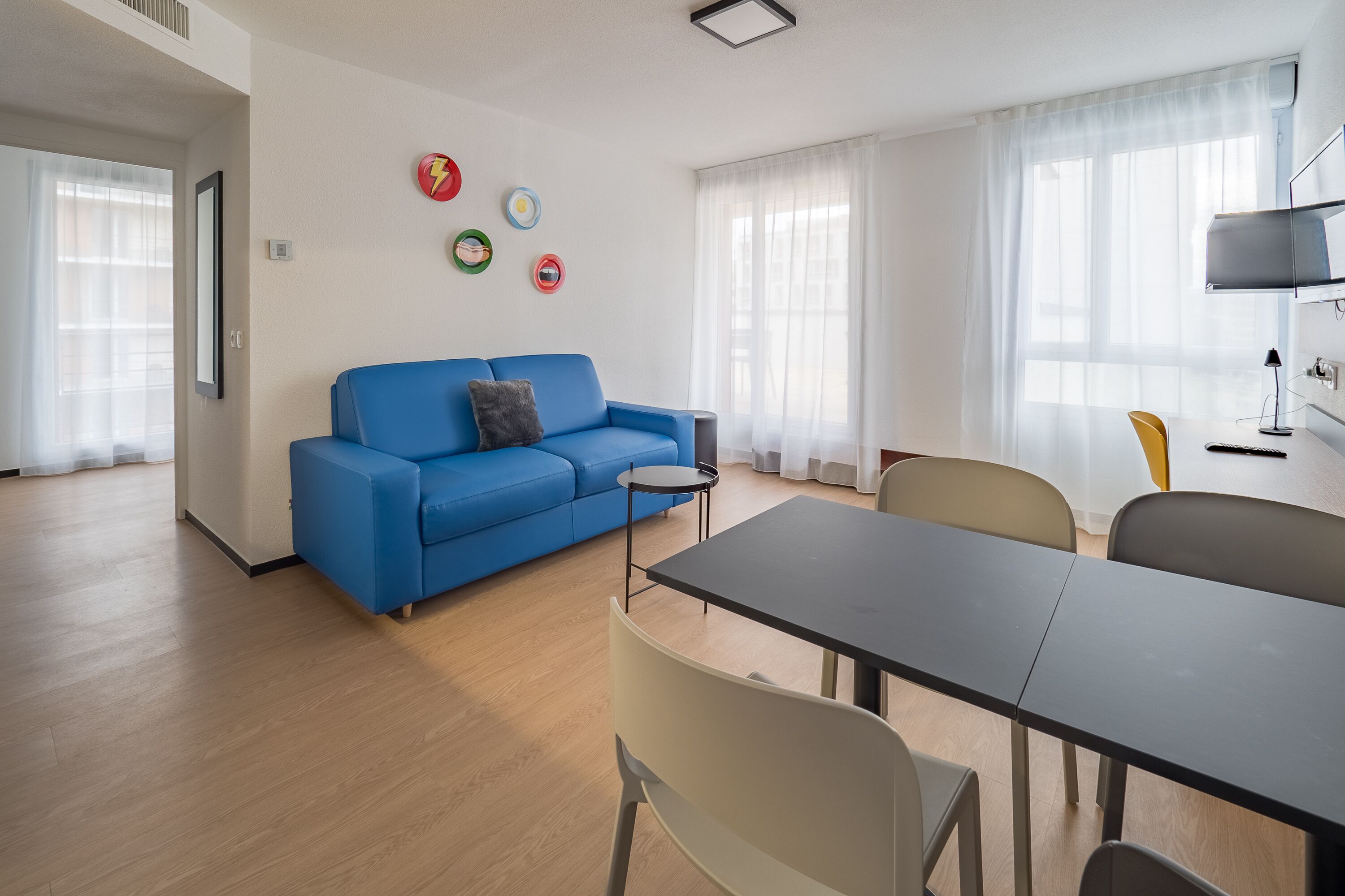A modern living room with a blue sofa, a small round table, and a dining table with chairs.