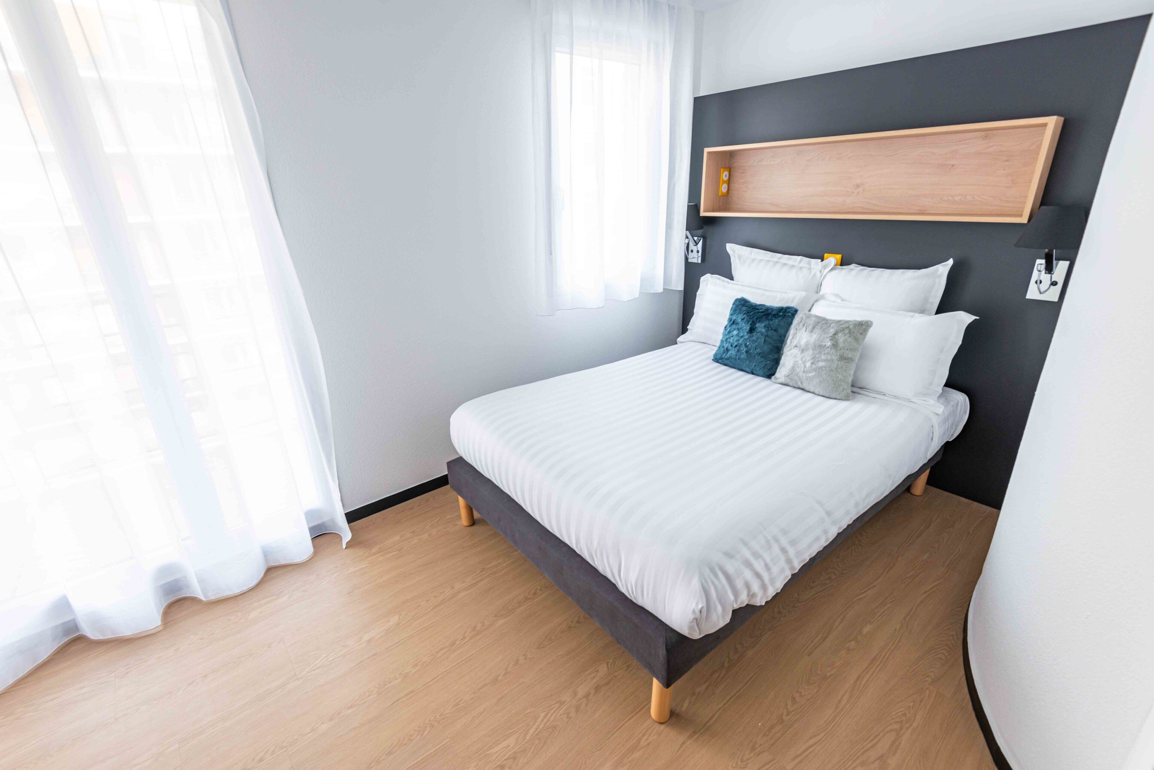 A modern bedroom with a bed, white bedding, and a wooden headboard.