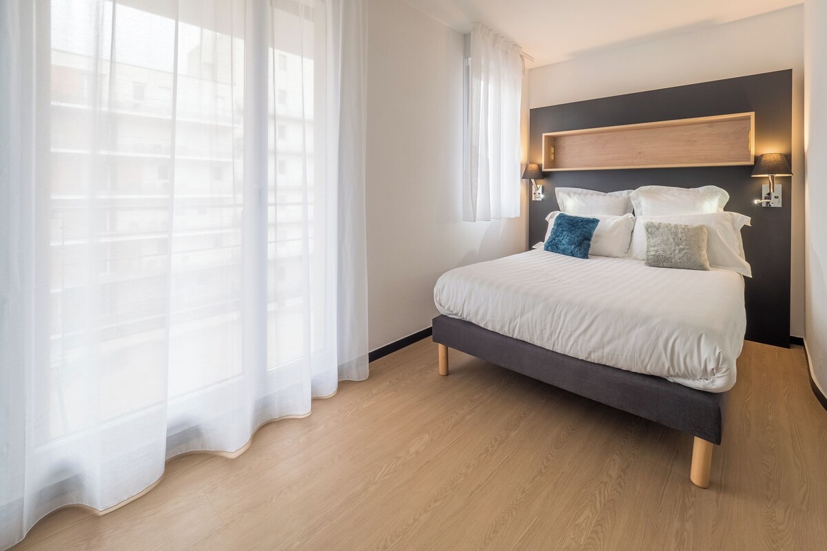 Quarto moderno com cama, cortinas e cabeceira com luzes embutidas.