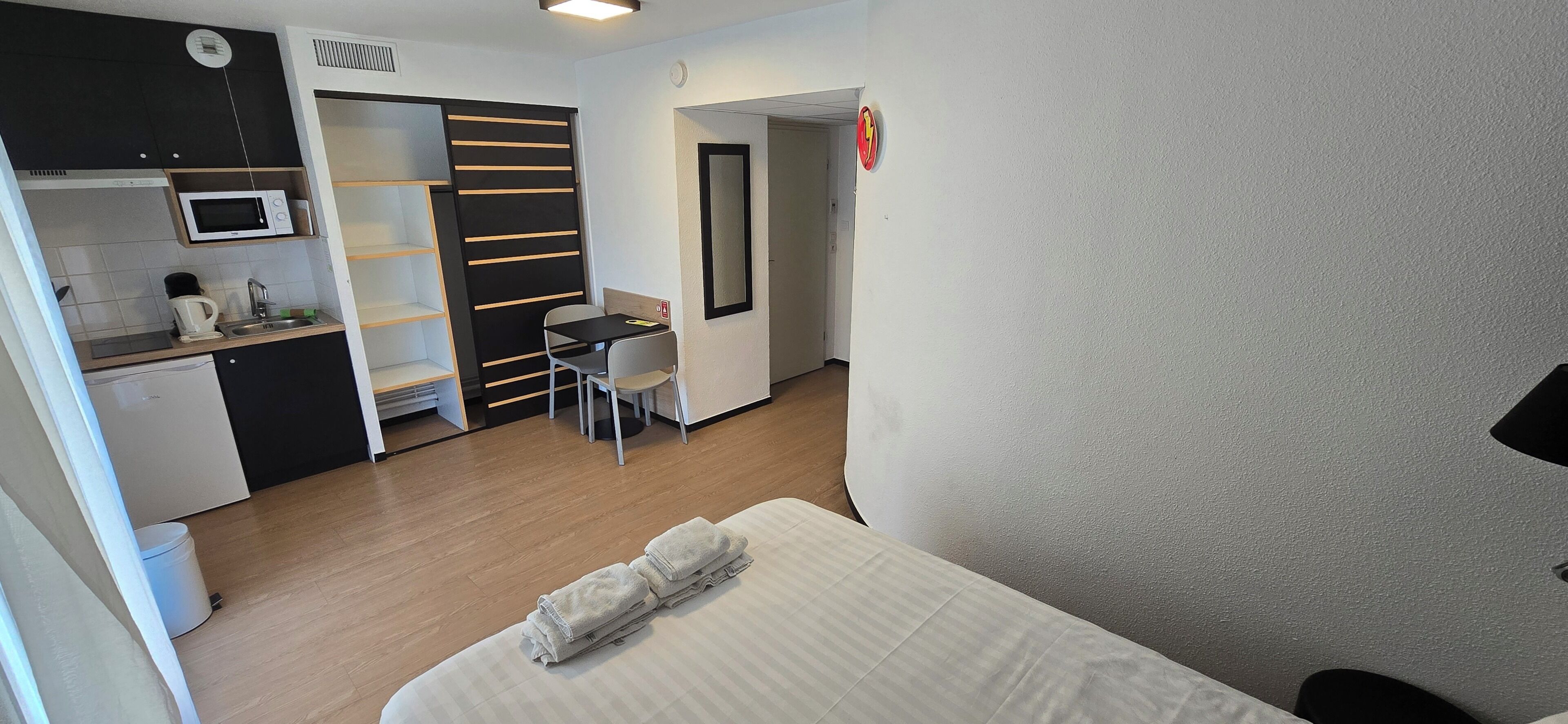 A compact hotel room with a bed, a small kitchenette, a dining area with a table and chairs, and a separate bathroom.