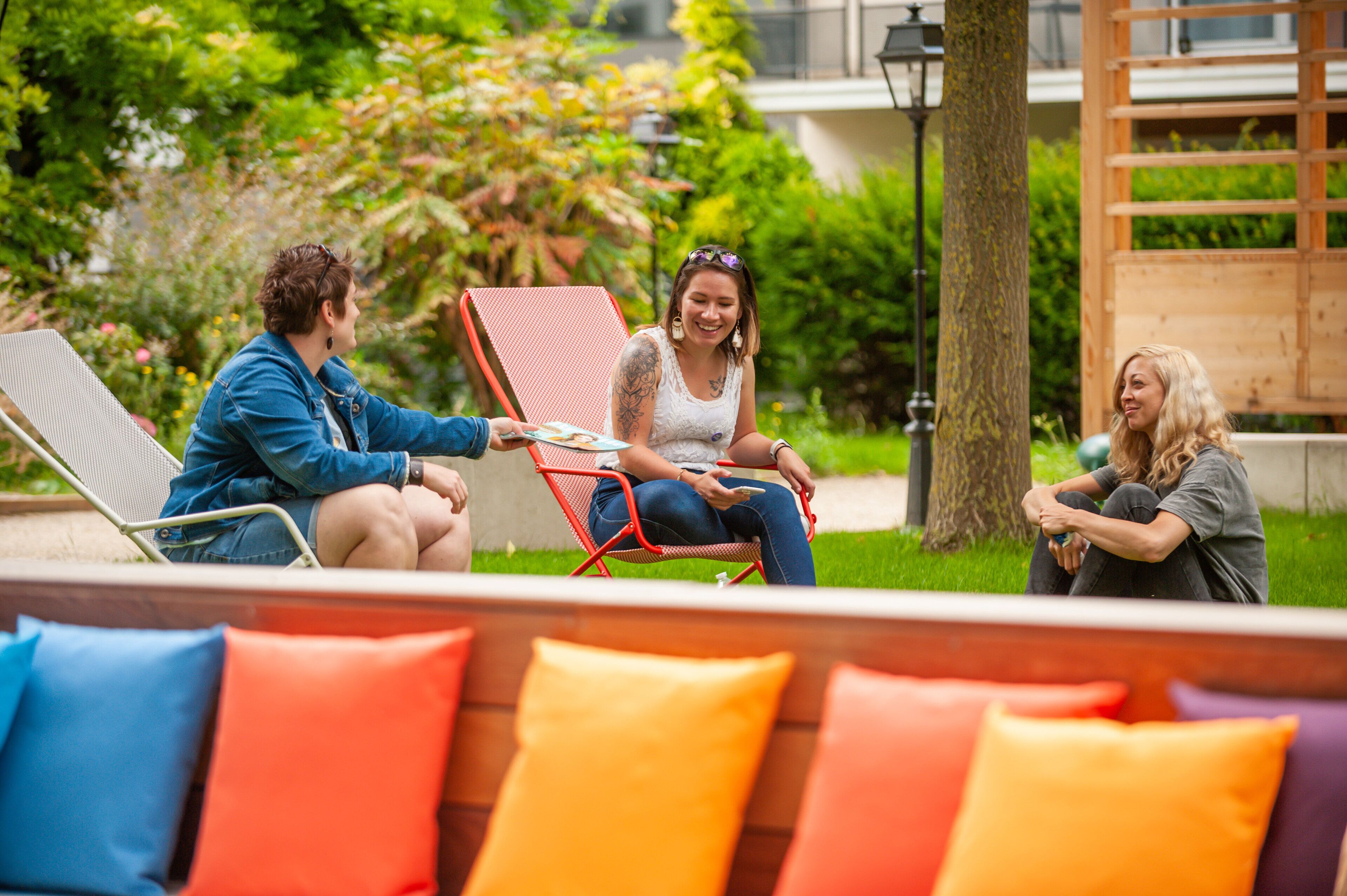 Drei Personen sitzen im Garten auf Gartenstühlen, im Hintergrund eine Holzhütte.