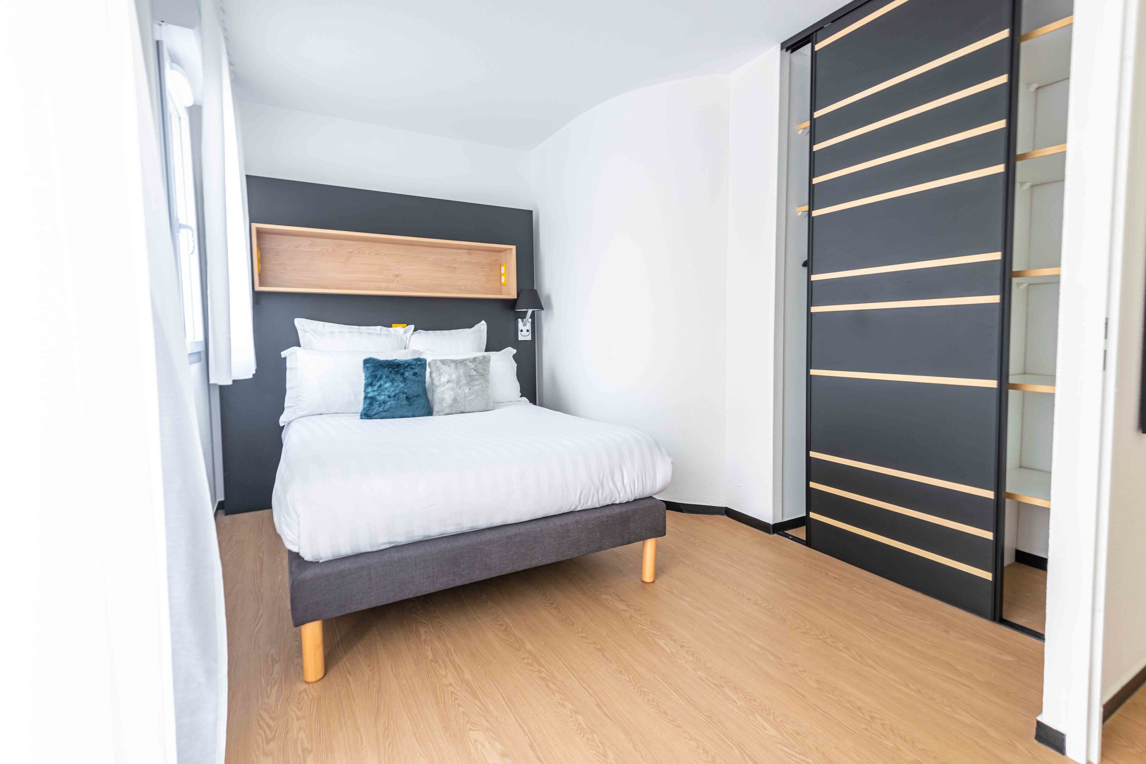 A modern bedroom with a bed, a wooden headboard, and a sliding door closet.