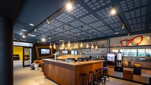 Zona de bar moderna con barra de madera, varios taburetes, lámparas colgantes y una variedad de utensilios y botellas de bar.