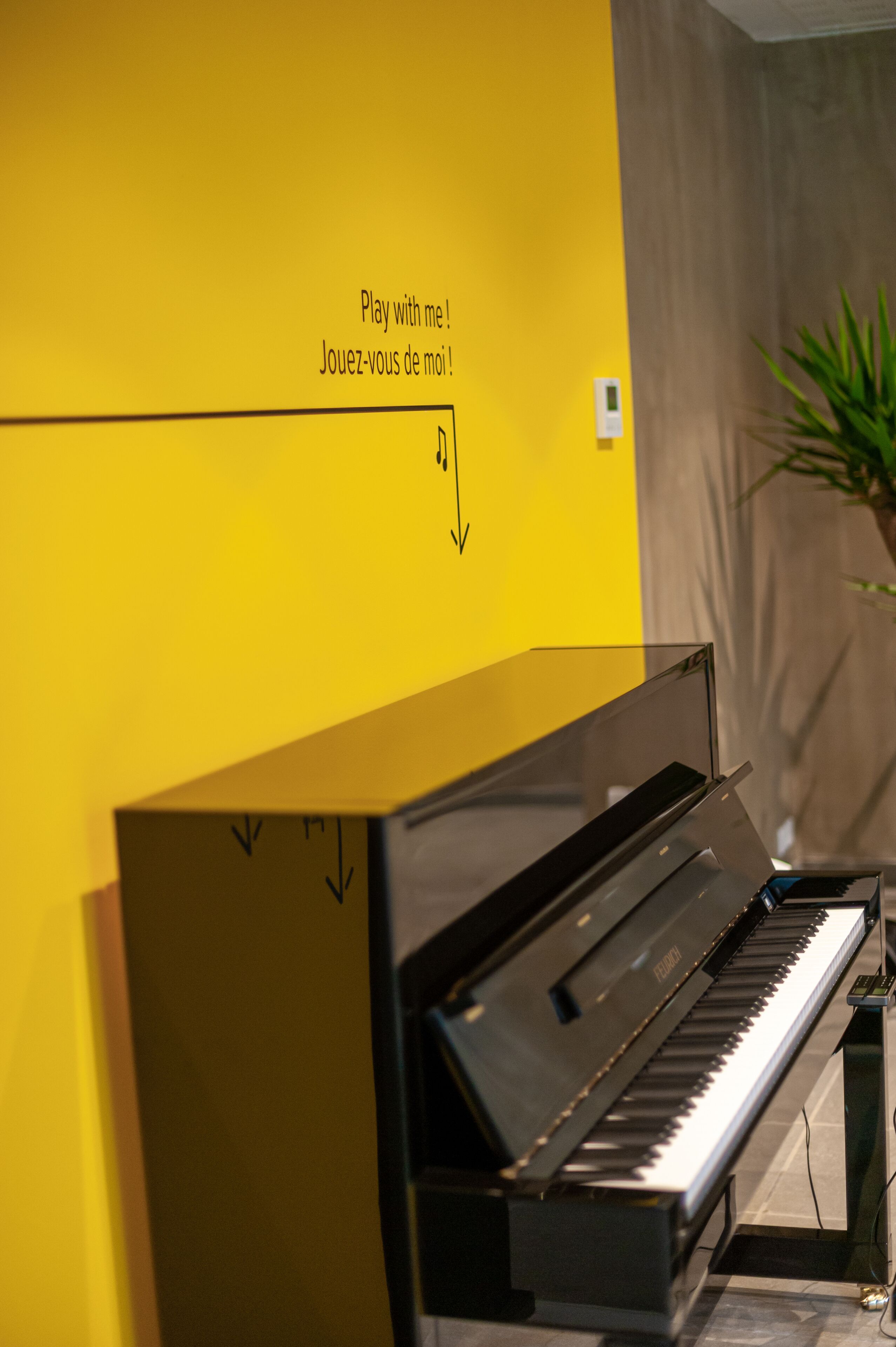 Un piano en una habitación con una pared amarilla y un letrero que dice “Juega conmigo”.