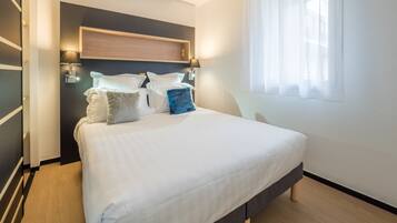 Ein modernes Schlafzimmer mit einem großen Bett, zwei Wandlampen und einem Fenster mit durchsichtigen Vorhängen.