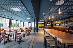 A modern restaurant with a bar area, large windows, and a patterned ceiling.