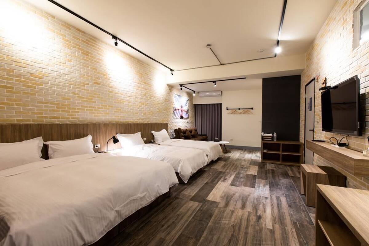 A hotel room with three beds, a TV, and a brick wall.