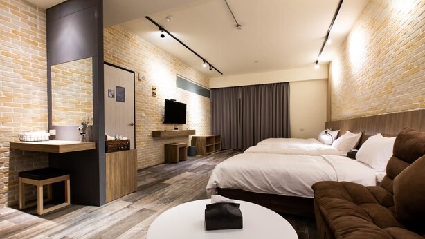 Una habitación de hotel moderna con pared de ladrillo, un televisor de pantalla plana, una cama grande, un sofá y una mesa de centro redonda.