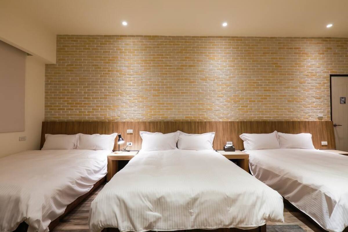 A hotel room with two beds, a brick-patterned wall, and a wooden headboard.
