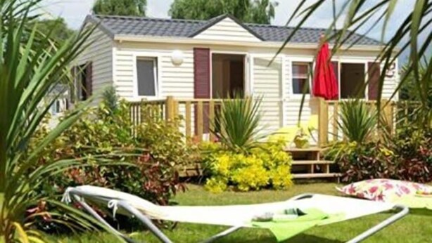 A single-story mobile home with a porch, surrounded by various plants and a hammock. - Campingplatz Jungferweiher (Ulmen)