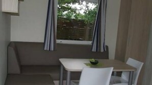 A small kitchenette with a refrigerator, a sink, and a window with curtains. - Campingplatz Jungferweiher (Ulmen)