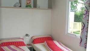 A small, clean room with two single beds, a window, and a shelf with items. - Campingplatz Jungferweiher (Ulmen)
