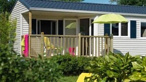 A single-story house with a covered porch, a small deck, and a green umbrella. - Campingplatz Jungferweiher (Ulmen)