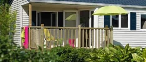 A single-story house with a covered porch, a small deck, and a green umbrella.