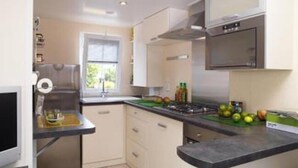 A modern kitchen with a built-in oven, a microwave, and a window providing natural light. - Campingplatz Jungferweiher (Ulmen)
