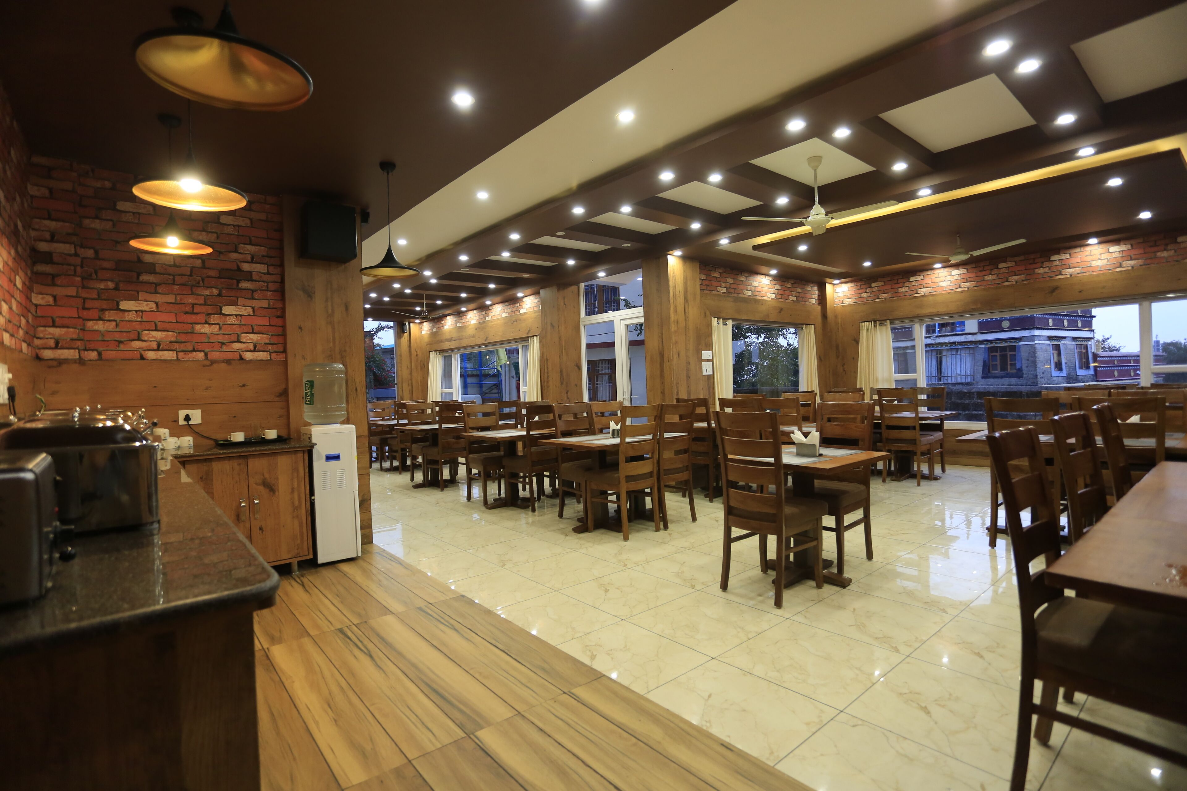 Un restaurant spacieux avec des tables et des chaises en bois, un mur en briques et un design moderne au niveau du plafond.