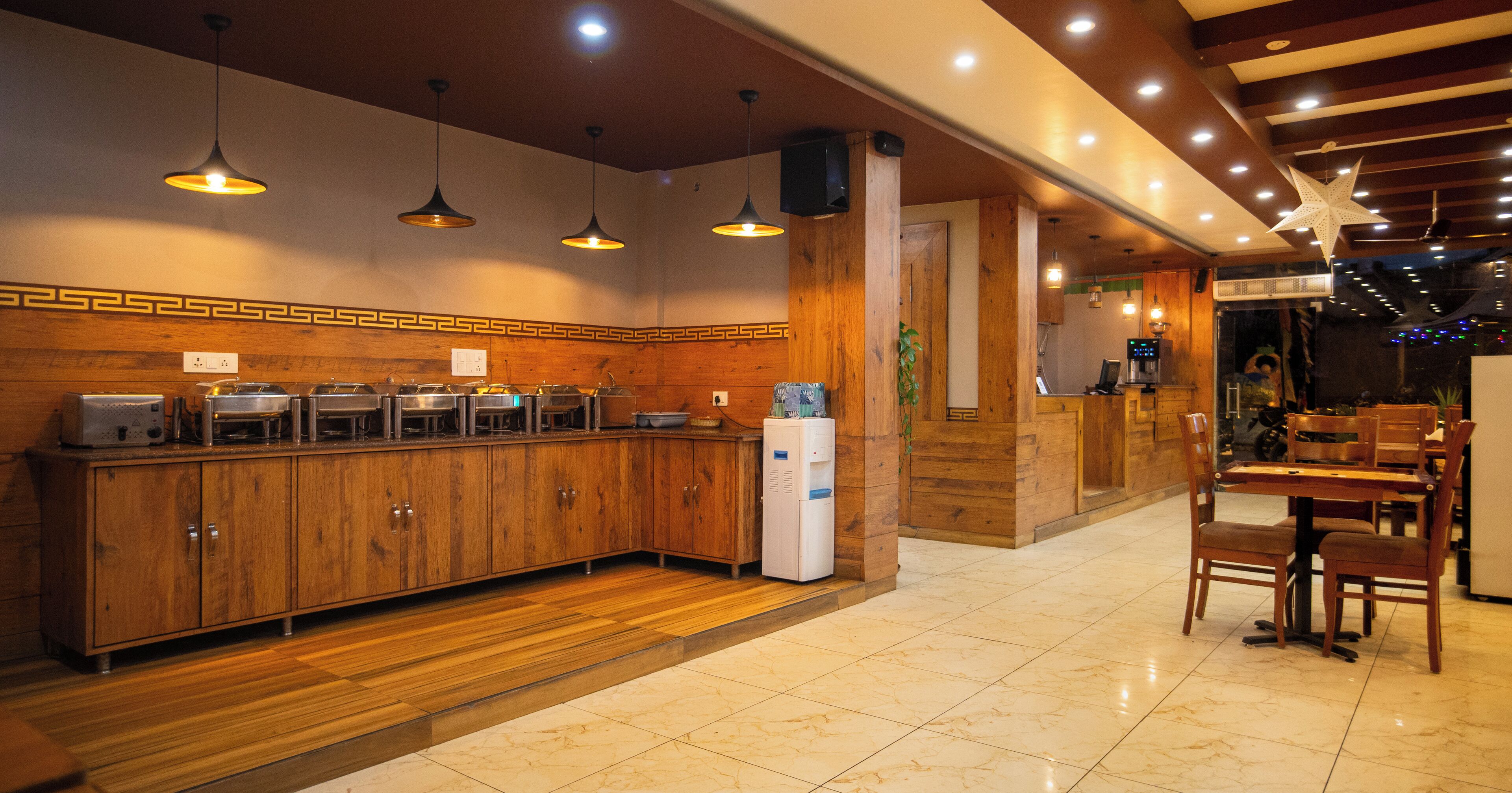 A restaurant with a long counter, wooden cabinets, hanging pendant lights, and a tiled floor.