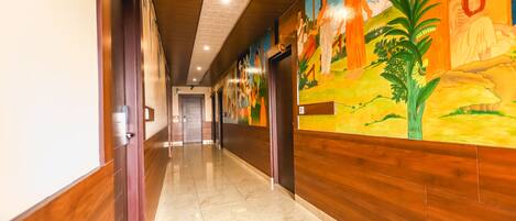 Un pasillo con paneles de madera, suelo de baldosas y un mural que representa figuras con vestimenta tradicional.