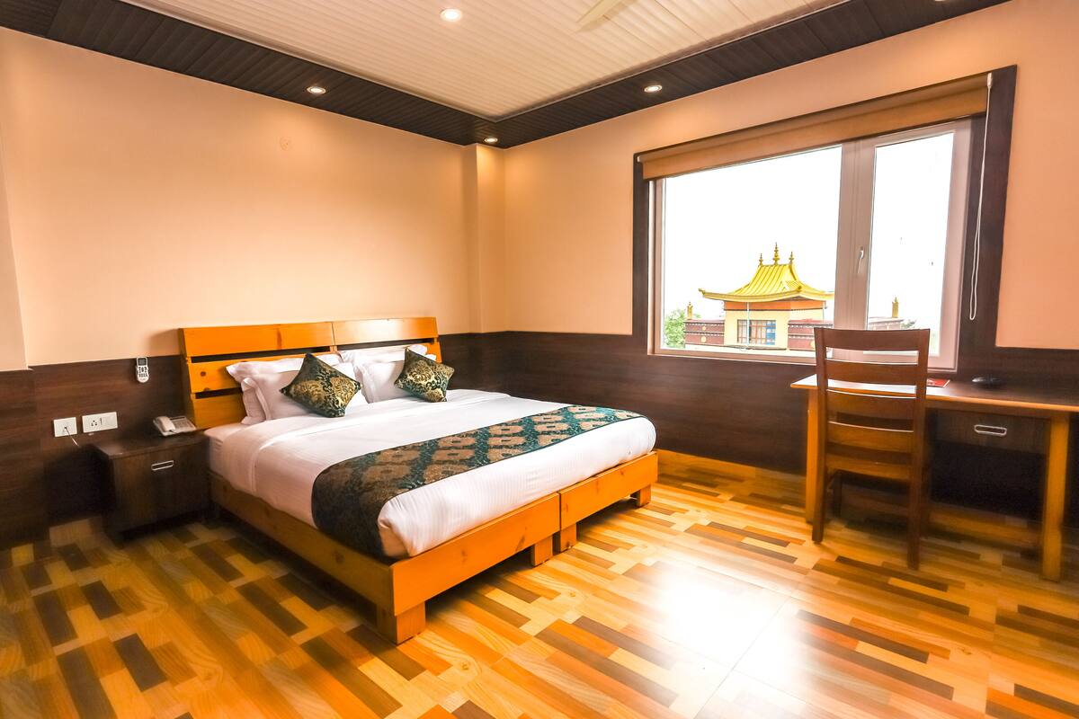 A hotel room with a wooden bed, a desk, and a window with a view of a building.