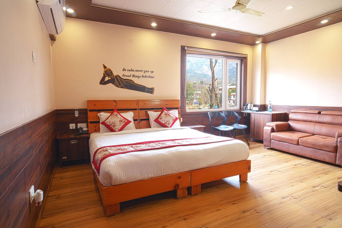 A hotel room with a wooden bed, a wooden headboard, a window with a mountain view, a brown leather sofa, and a wall with a motivational quote.