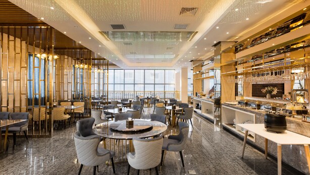 Een ruime hotellobby met een hoge plafond, moderne kroonluchters en een bar.