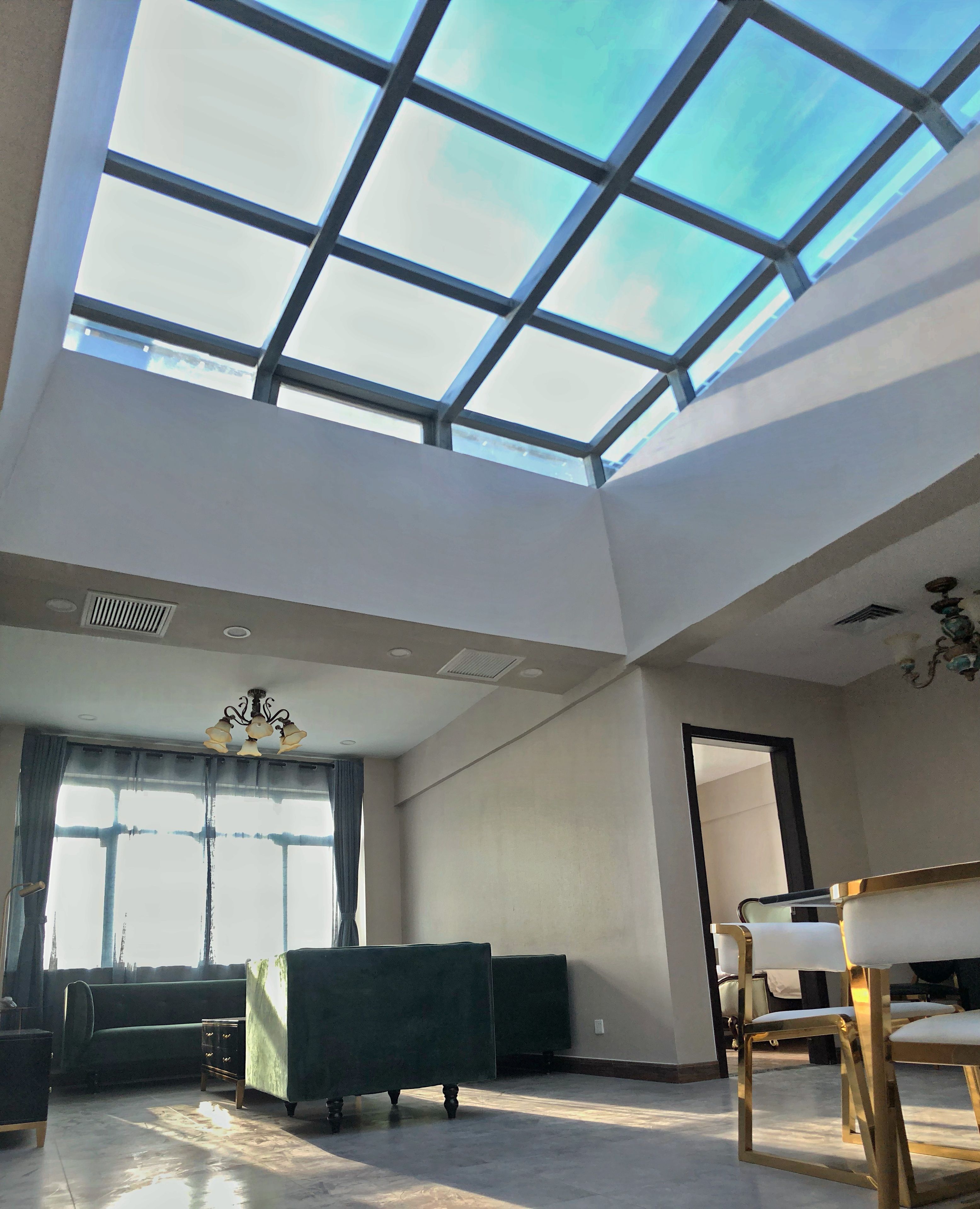 A spacious room with a skylight, a green sofa, a dining table with chairs, and a chandelier.