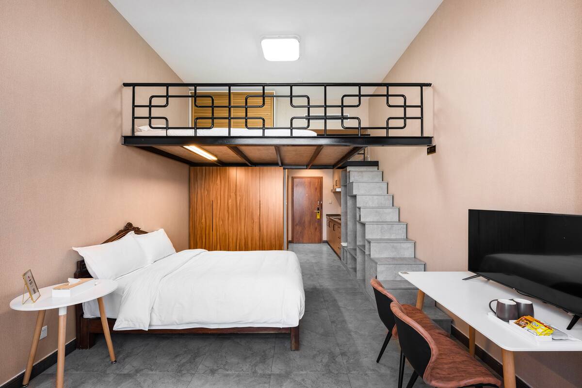 Ein Schlafzimmer mit Etagenbett, Schreibtisch mit Stuhl, Fernseher und Treppe.