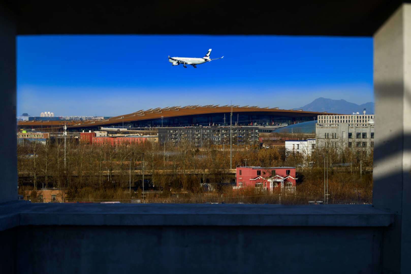 An airplane flying over a cityscape with a stadium and buildings in the background.