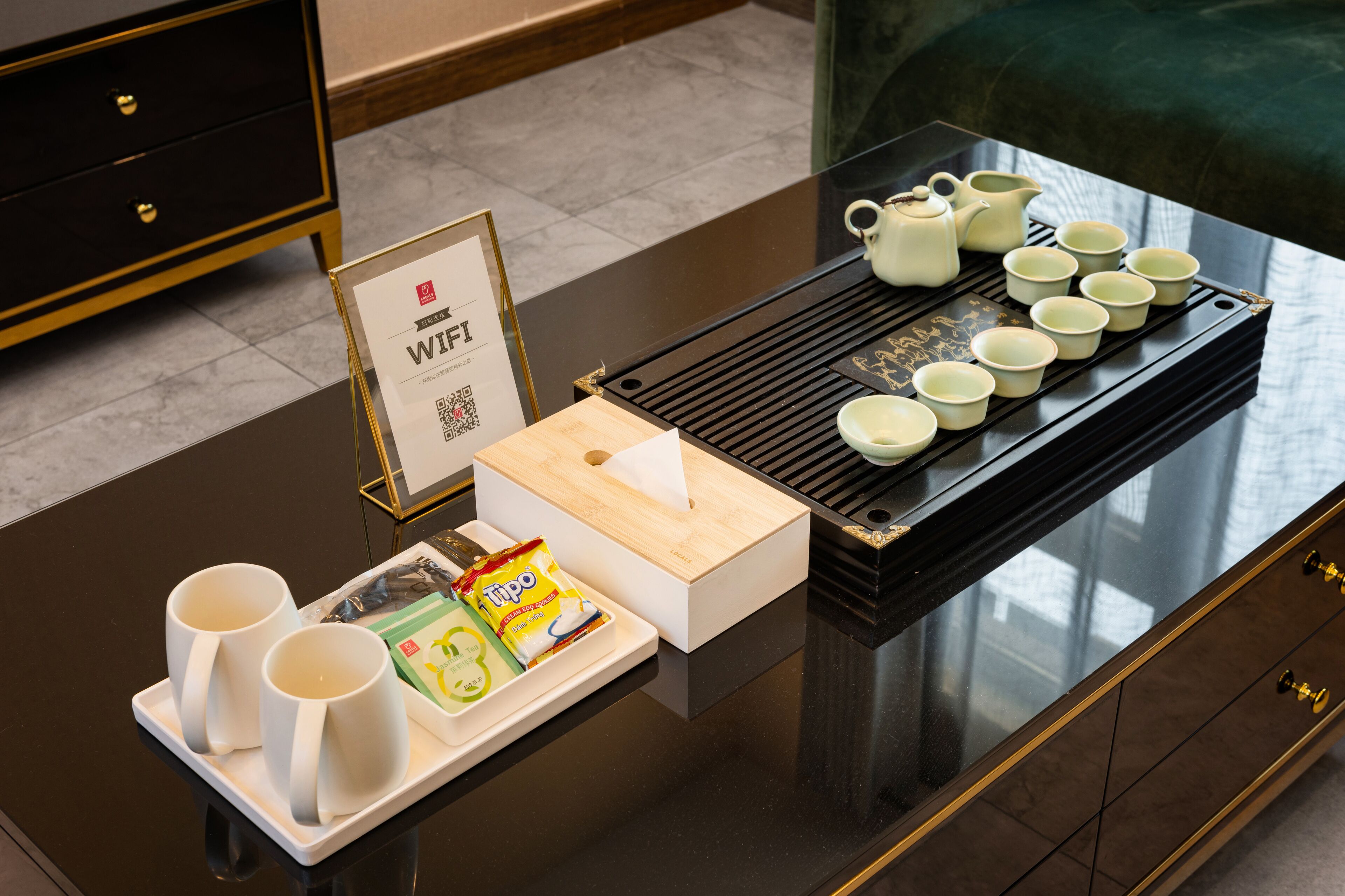 Habitación de hotel con una mesa negra dispuesta para servicio de té, incluyendo tazas, tetera y bandeja con tazas de té.