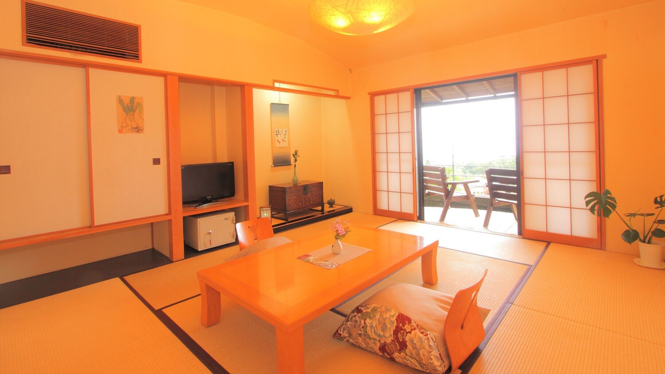 A traditional Japanese room with tatami flooring, a television, a cabinet, and a sliding door leading to a balcony.