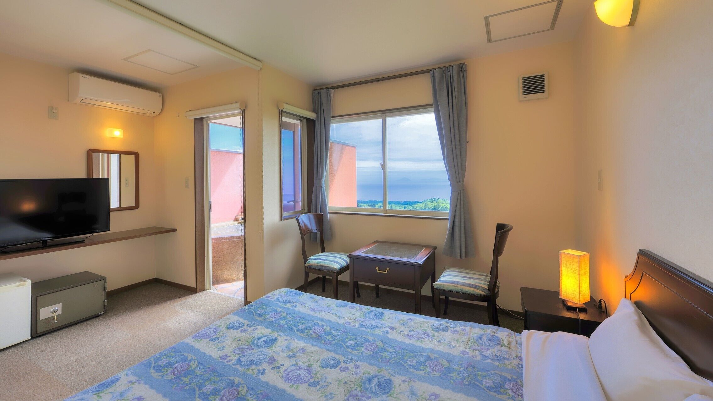 A hotel room with a bed, a desk, a chair, a television, a safe, and a window with a view.