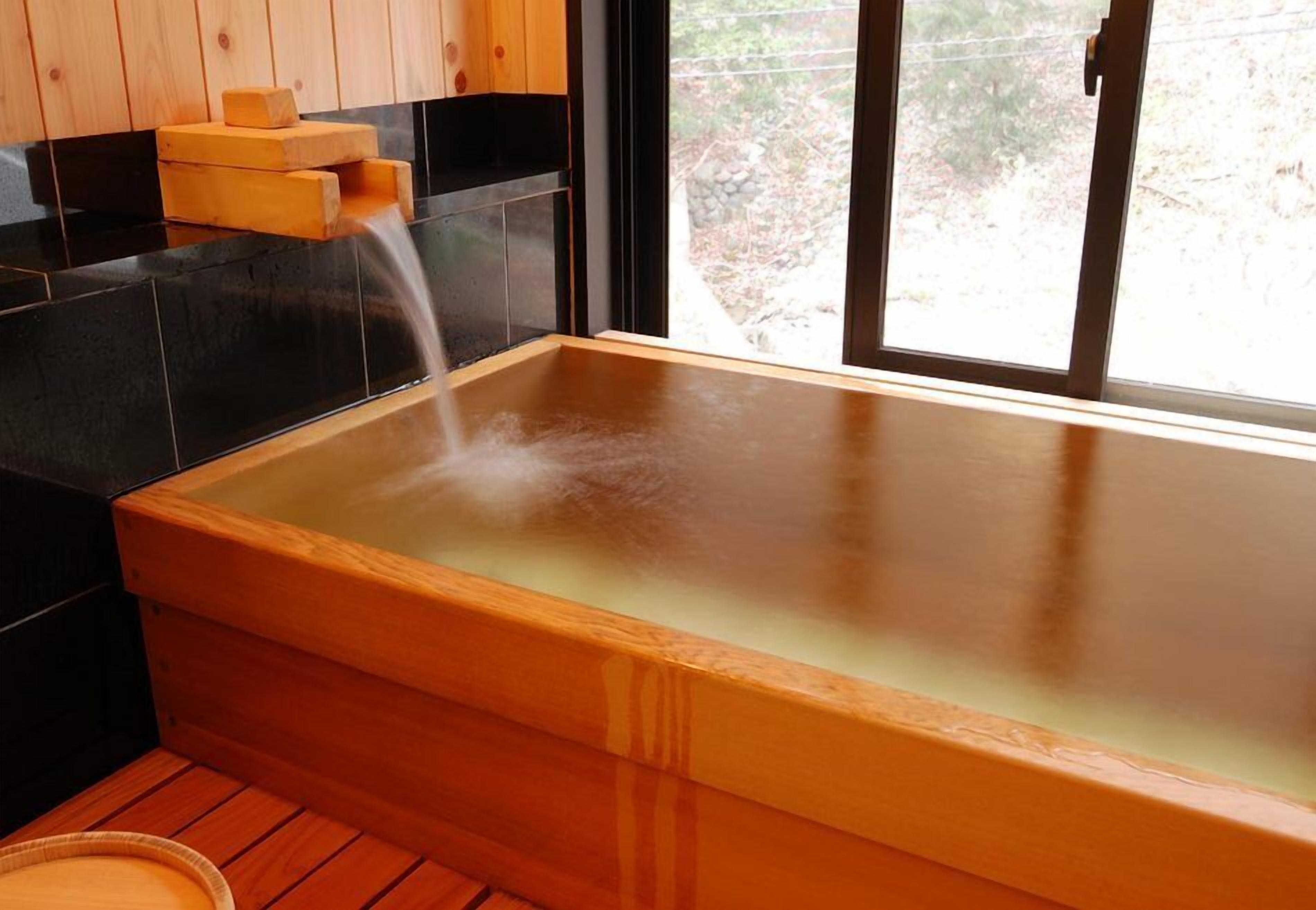 Un bain à remous en bois offrant une vue dégagée sur l’extérieur grâce à une fenêtre.