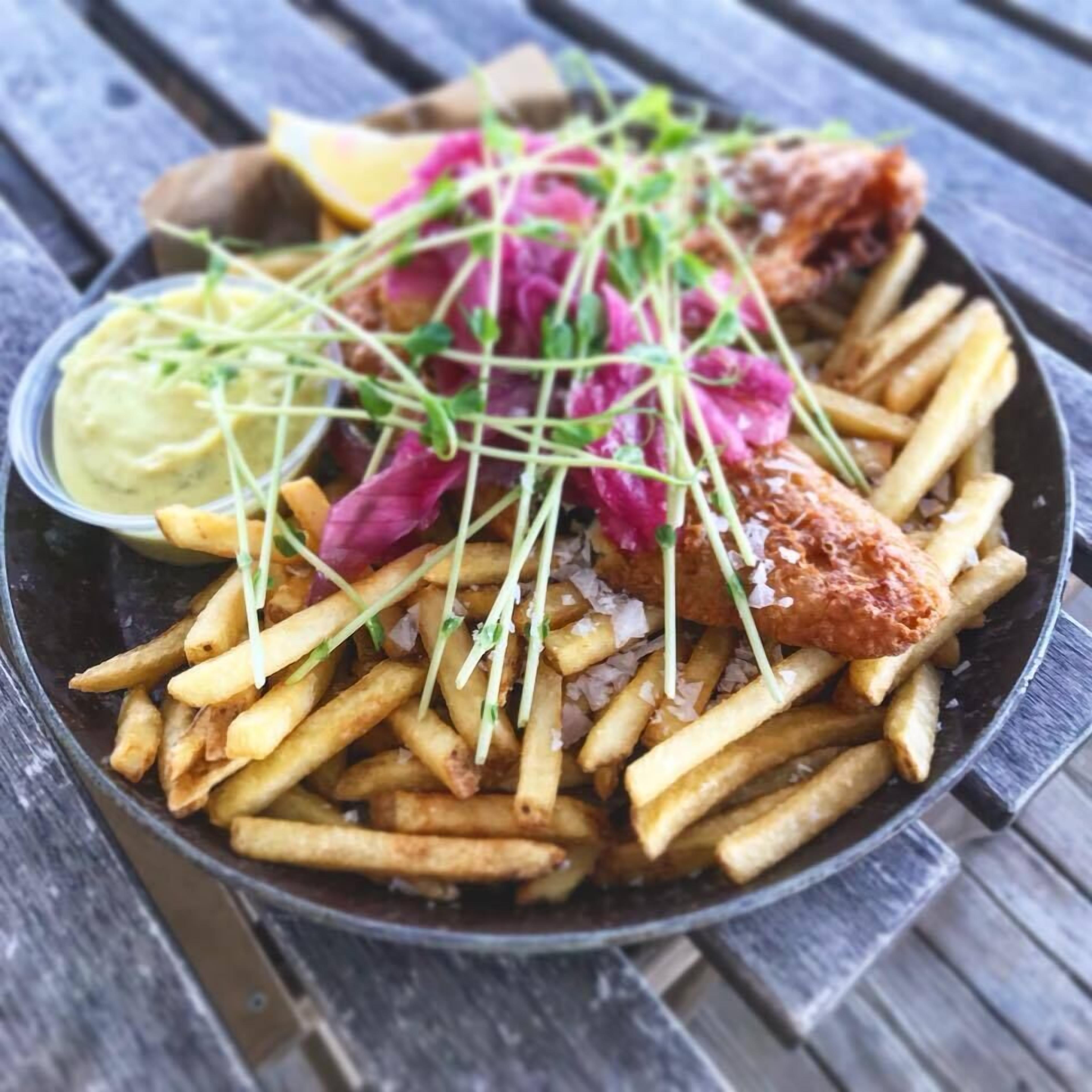 A meal consisting of fries, a fried fish, and a side of sauce on a wooden table.