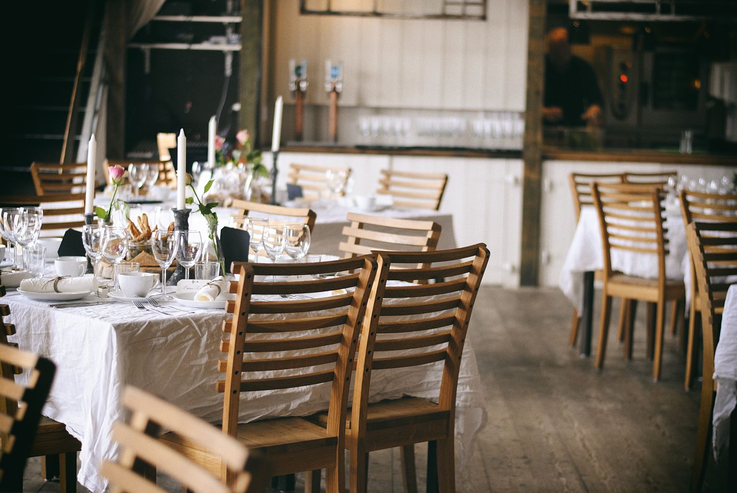 Un restaurante con sillas y mesas de madera dispuestas para comer, con manteles blancos y cristalería.