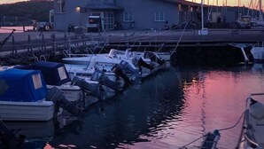 Una marina con barcos amarrados, un edificio con varias ventanas, e una bandera en un asta.