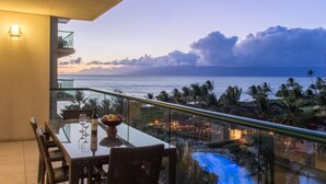 Ein Balkon mit Glastisch und Stühlen mit Blick auf einen Pool und den Ozean.