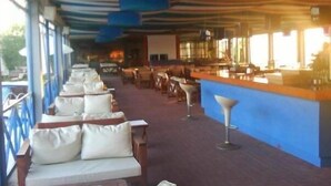 A covered outdoor seating area with rows of white cushioned benches and a bar counter. - Ocean-Pacific (Pyrgos)