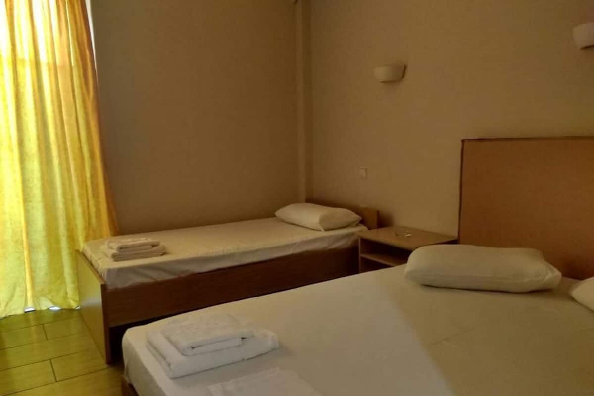 Een kleine, schone kamer met twee bedden, een houten hoofdbord en een nachtkastje met een lamp.