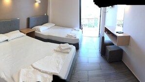 A hotel room with two beds, a small seating area, and a window providing a view of the outdoors. - Ocean-Pacific (Pyrgos)