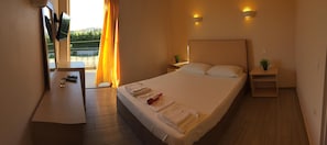Una habitación de hotel con una cama grande, mesitas de noche, un escritorio pequeño y una ventana con cortinas.