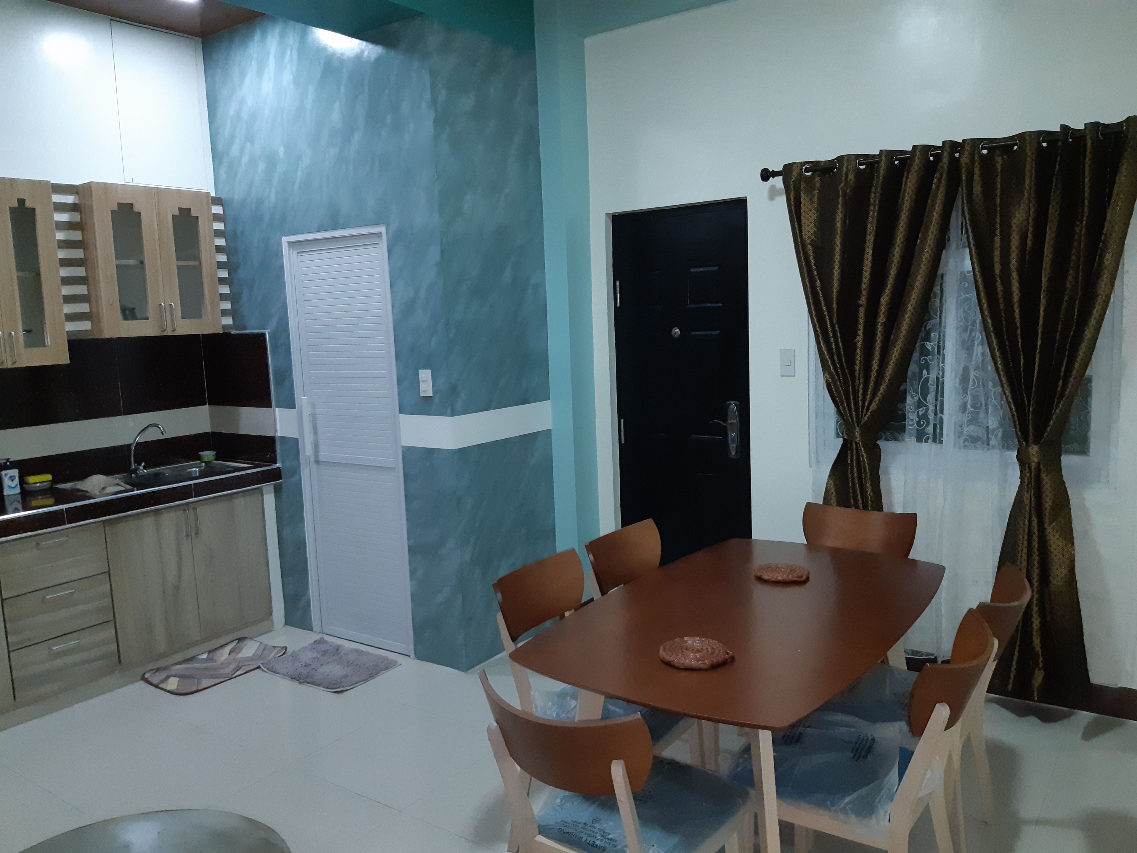 Un comedor con mesa y sillas, una cocina con armarios, una puerta y una ventana con cortinas.